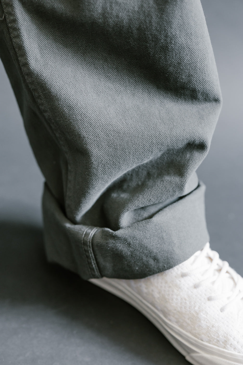 Close-up of gray pants with white sneakers on a neutral background