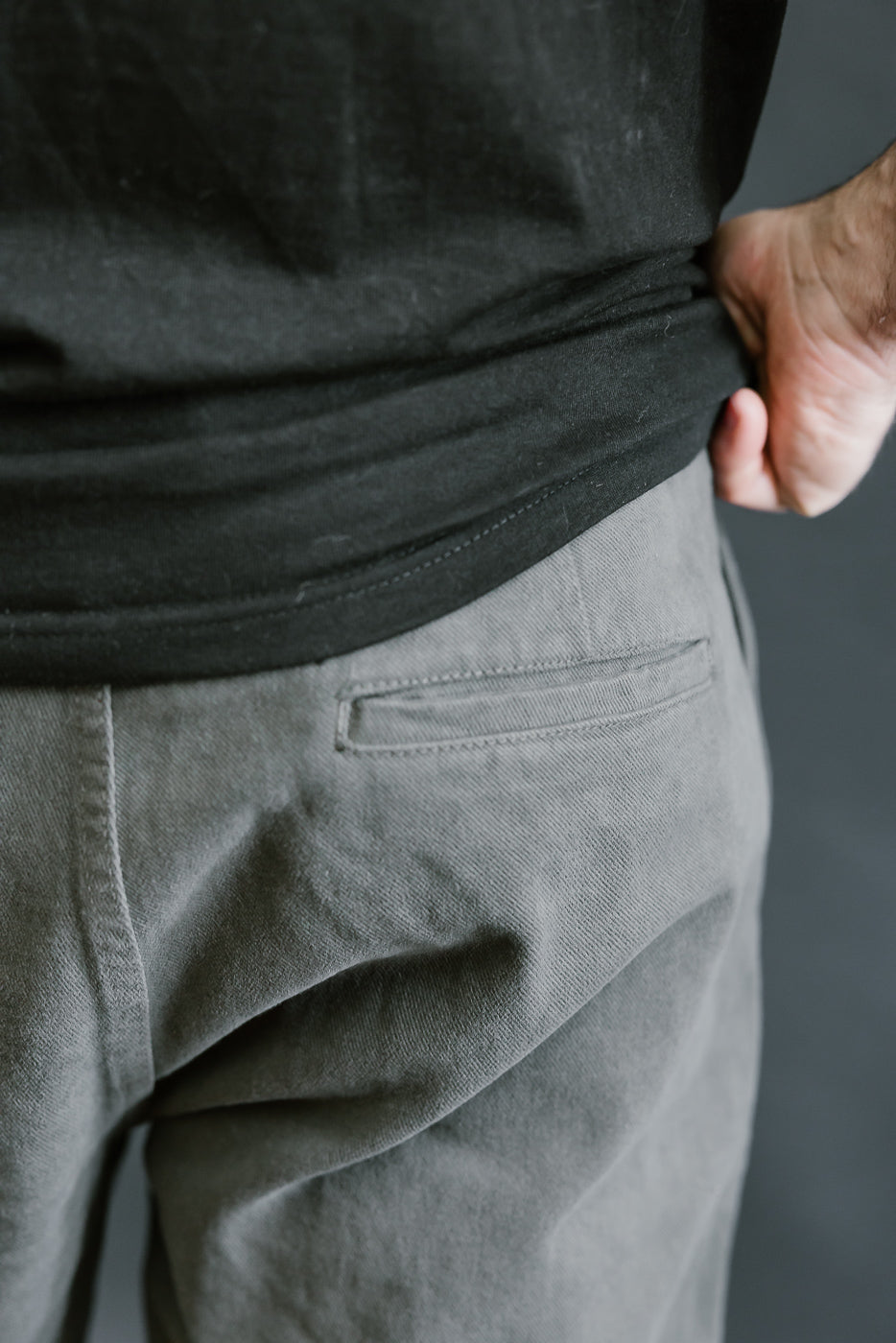 Person wearing a black shirt and gray pants against a neutral background