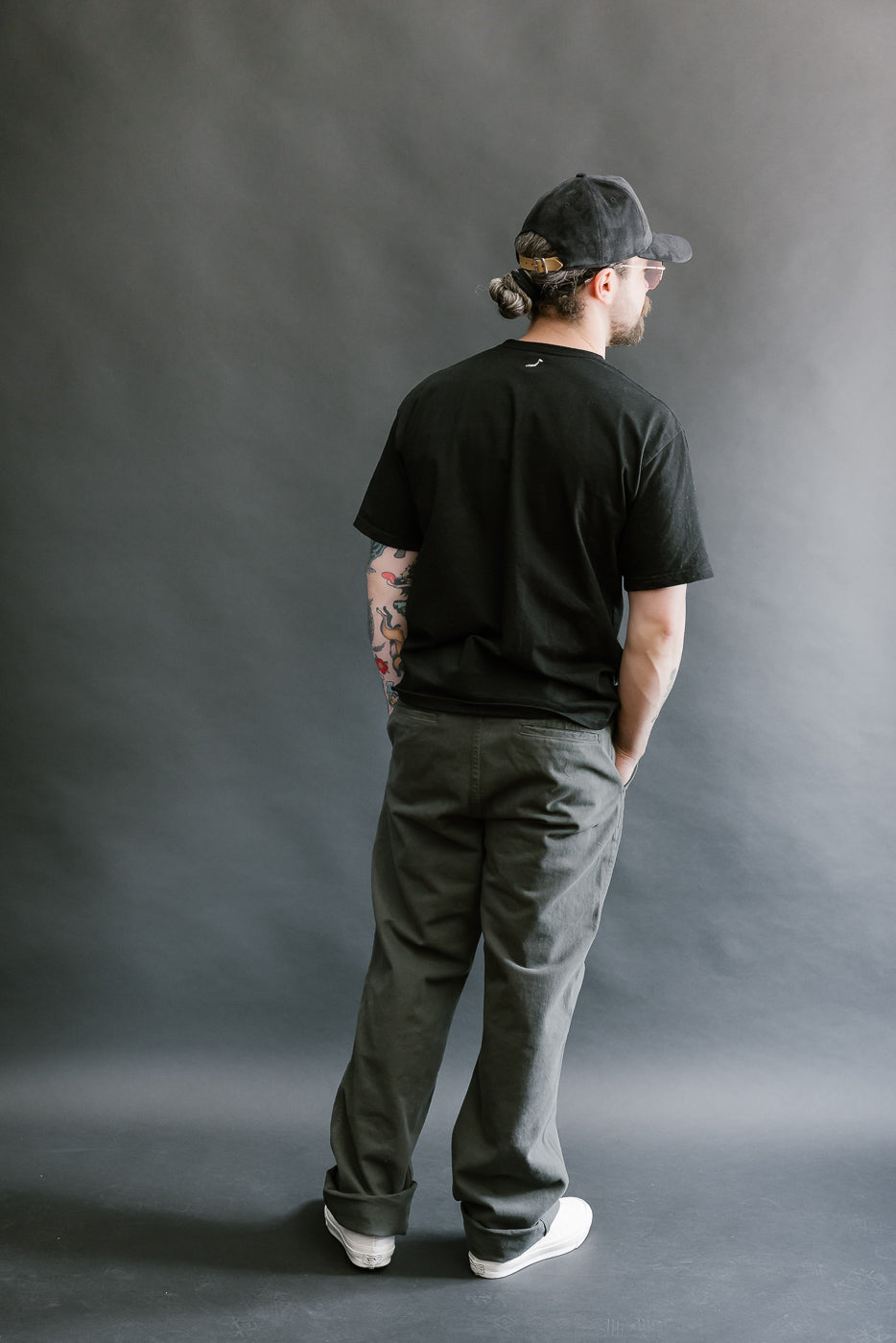 Person wearing a black t-shirt, cap, and pants against a gray background