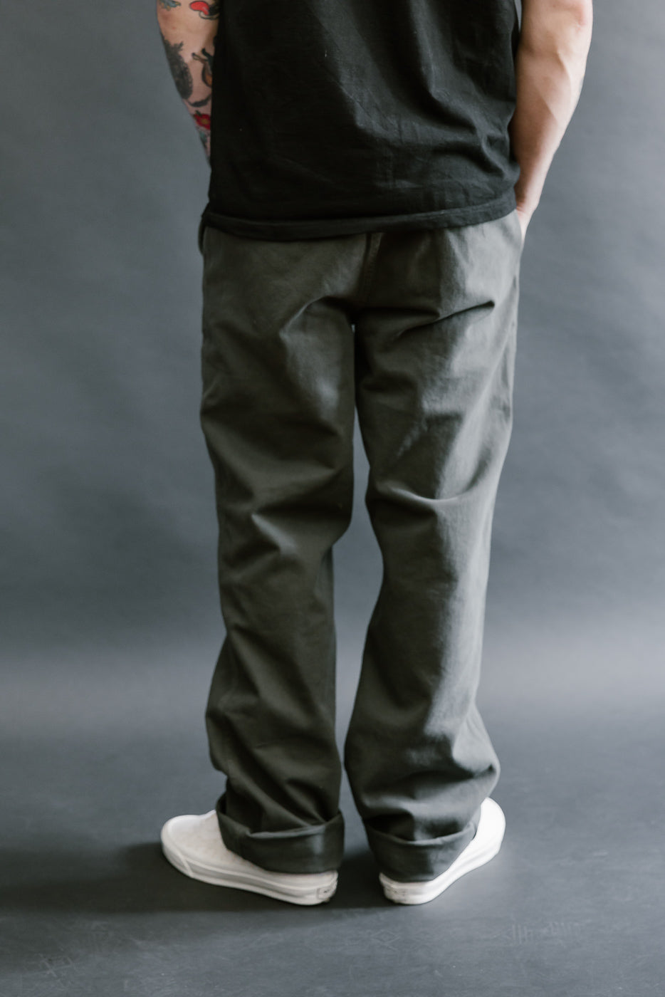 Person wearing a black sleeveless shirt and dark pants against a gray background