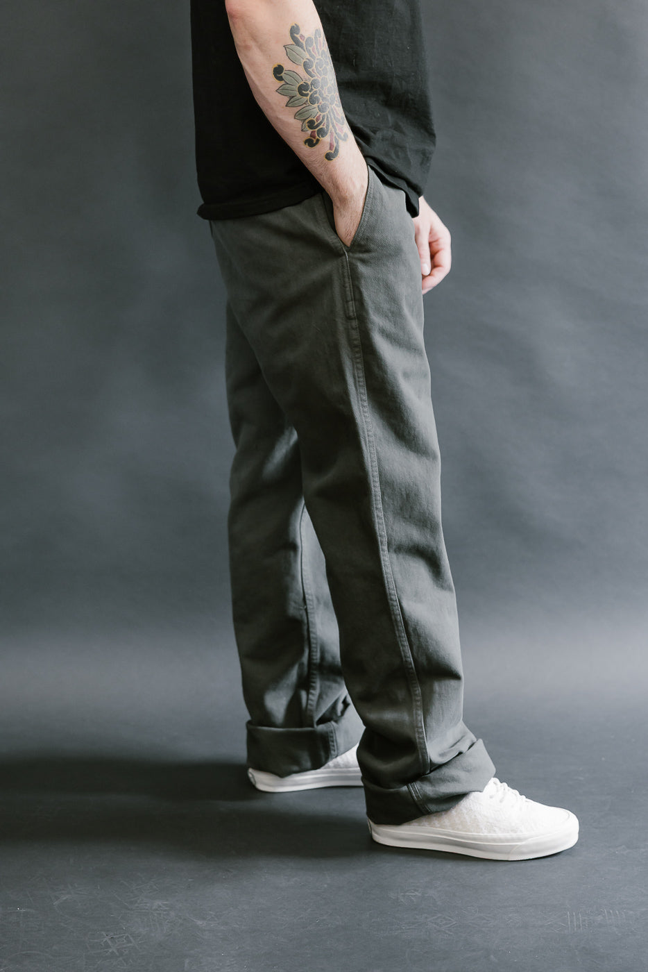 Person wearing dark gray pants and white sneakers on a gray background