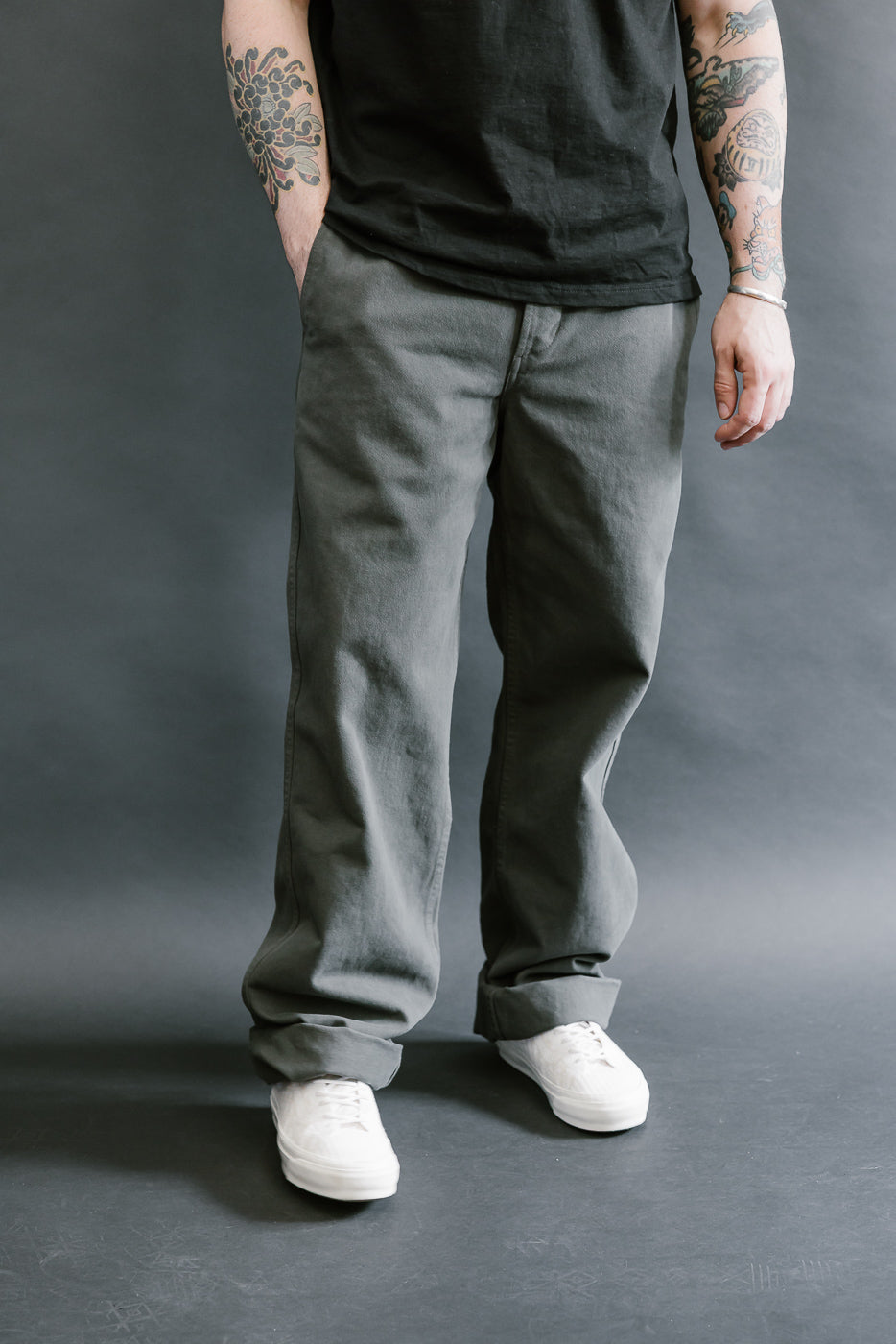 Person wearing gray pants and a black shirt against a gray background