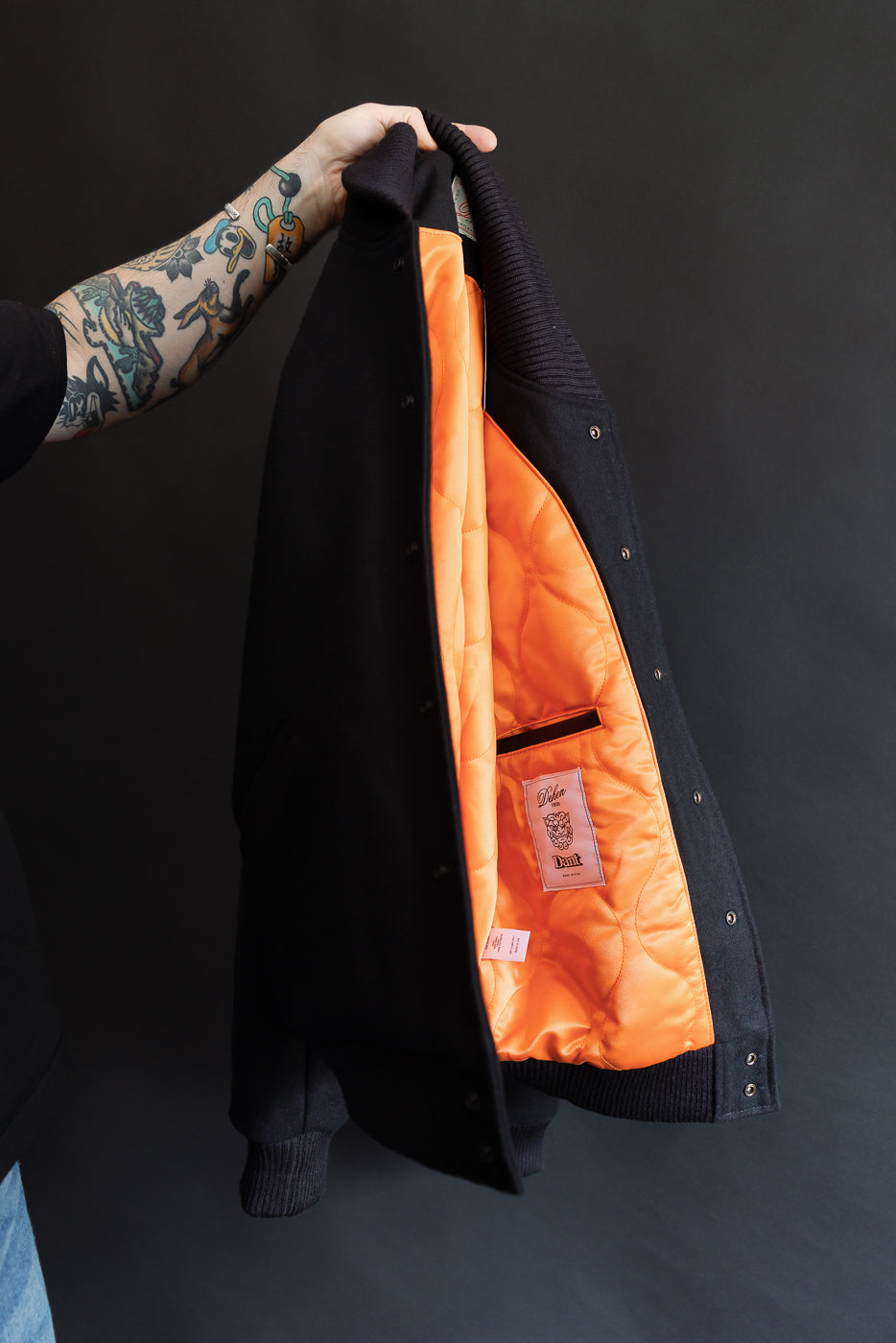 man holding black wool jacket in the air exposing the orange satin liner