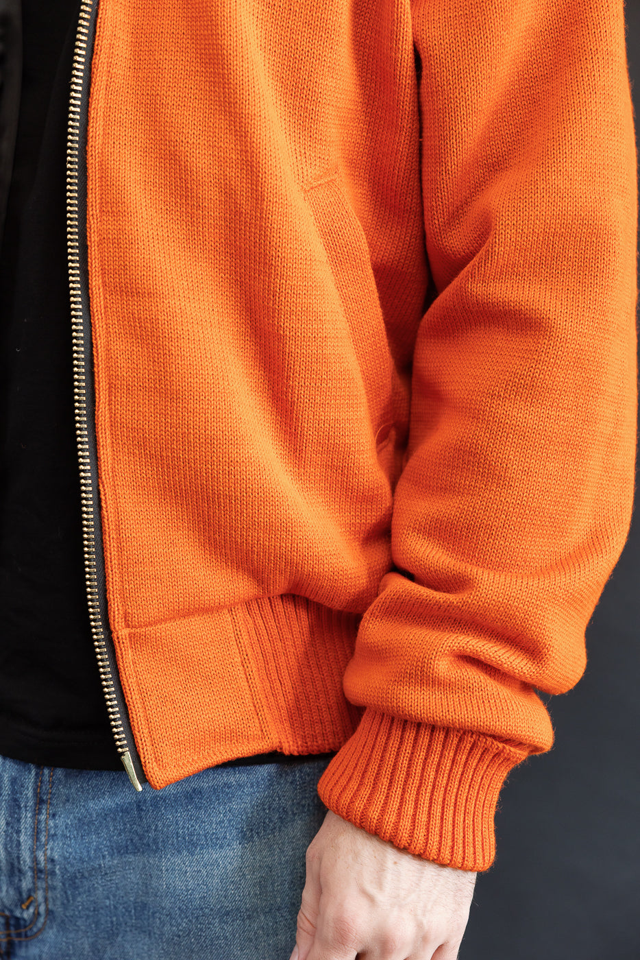 Male model wearing a knitted orange hoodie (open), black shirt, close up, hem and sleeve opening