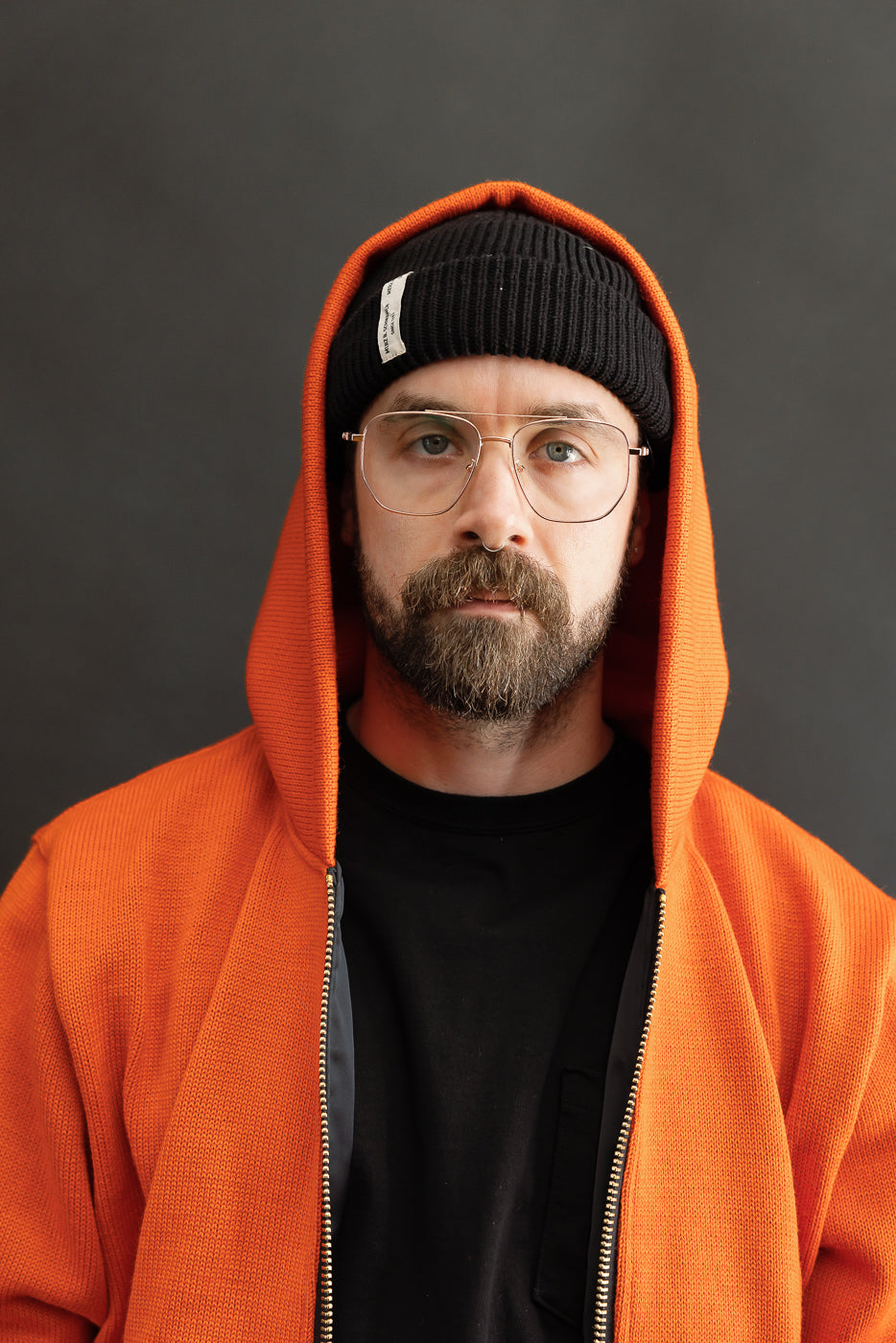 Male model wearing a knitted orange hoodie (open), black beanie, black shirt, close up, front view, hood up