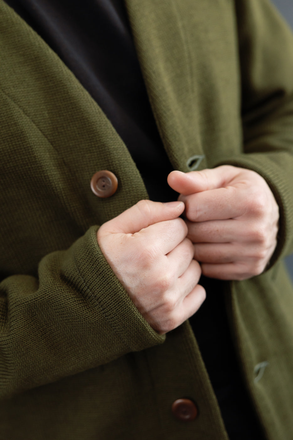 close up of placket of olive green cardigan with brown corozo buttons, black t-shirt underneath