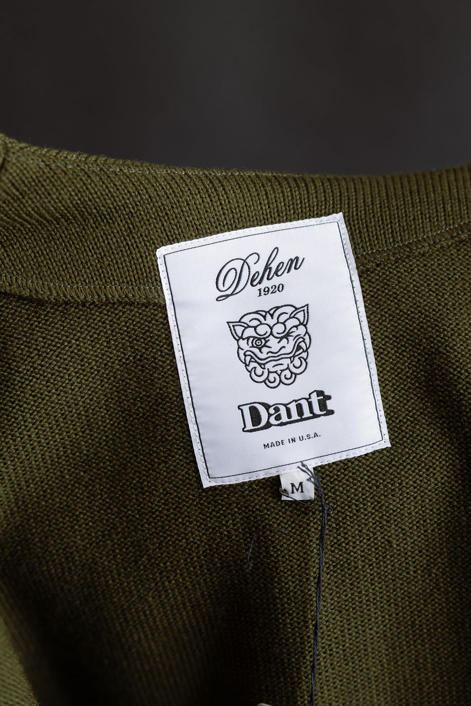 close up of dehen x dant logo with a gargoyle illustration in the center on white tag