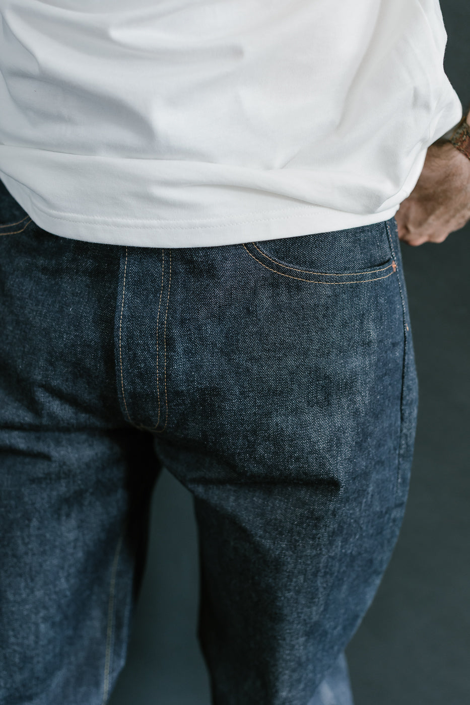 Person wearing blue jeans and a white shirt with a dark background