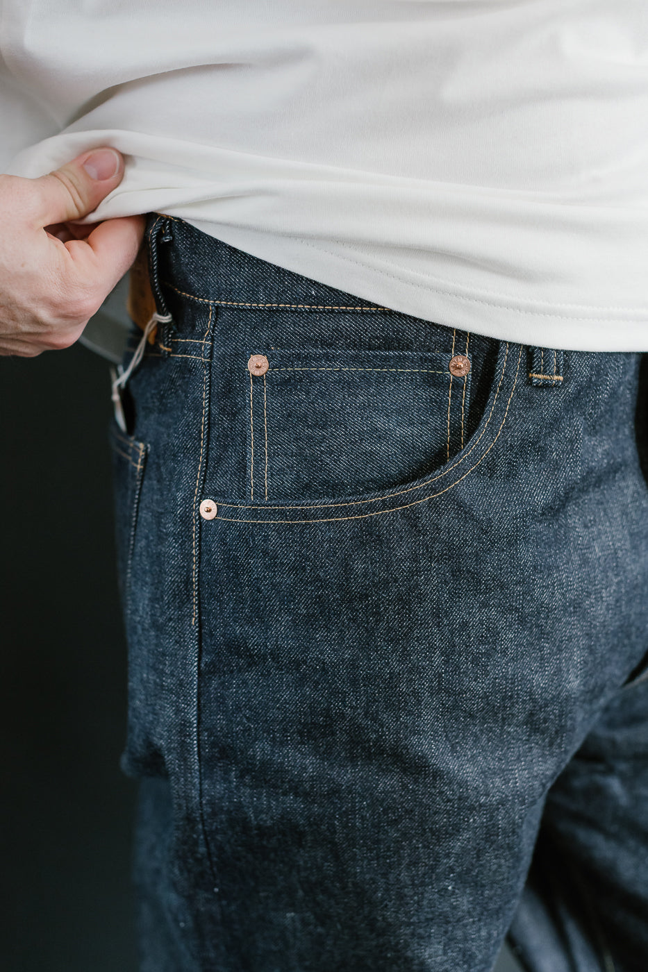 Person wearing blue jeans with a white shirt, focusing on the waistband.