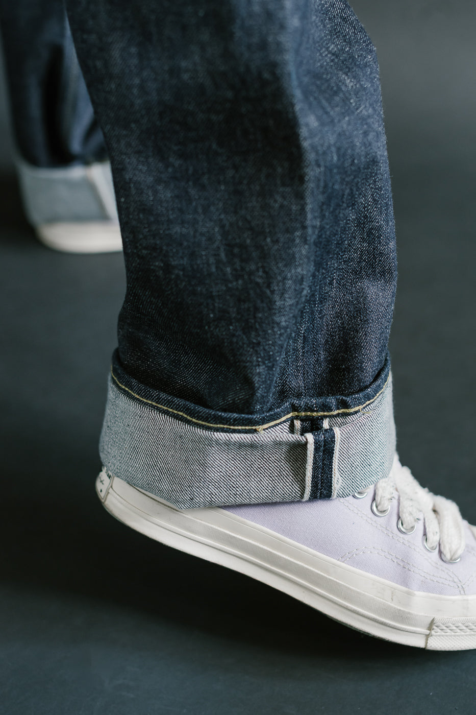 Close-up of a person wearing dark blue jeans and gray sneakers on a dark background