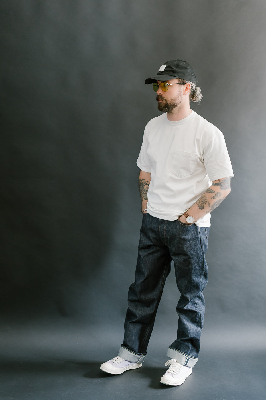 Man wearing a white t-shirt, black cap, and dark jeans against a gray background