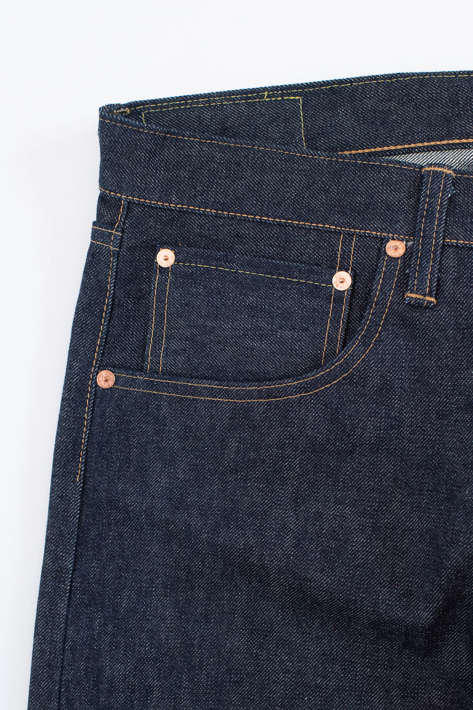 Close-up of dark blue denim jeans with button and zipper details on a white background