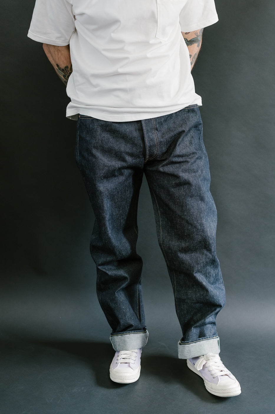 Person wearing a white shirt and blue jeans against a dark background