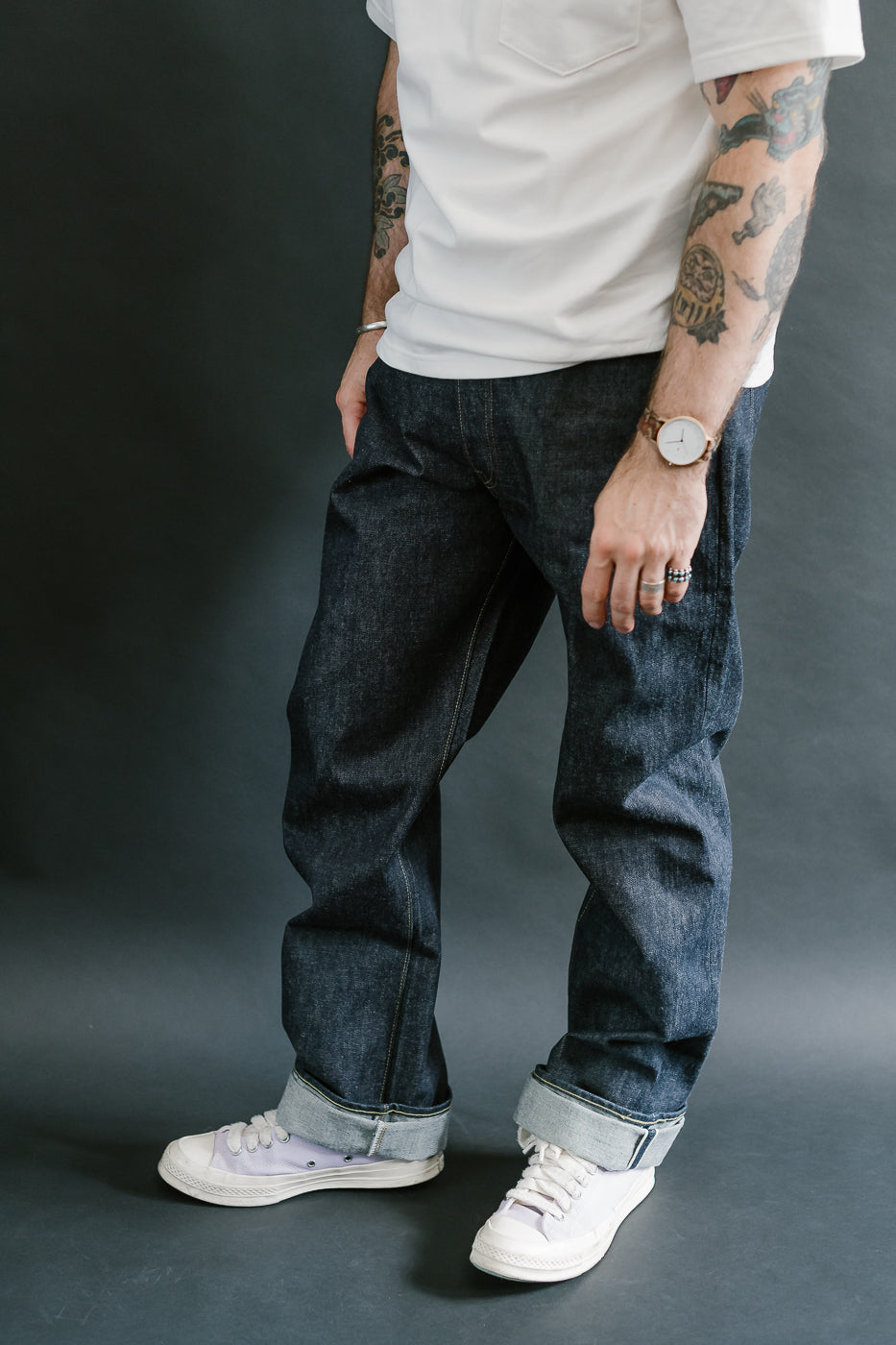Person wearing a white t-shirt, dark jeans, and white sneakers against a gray background