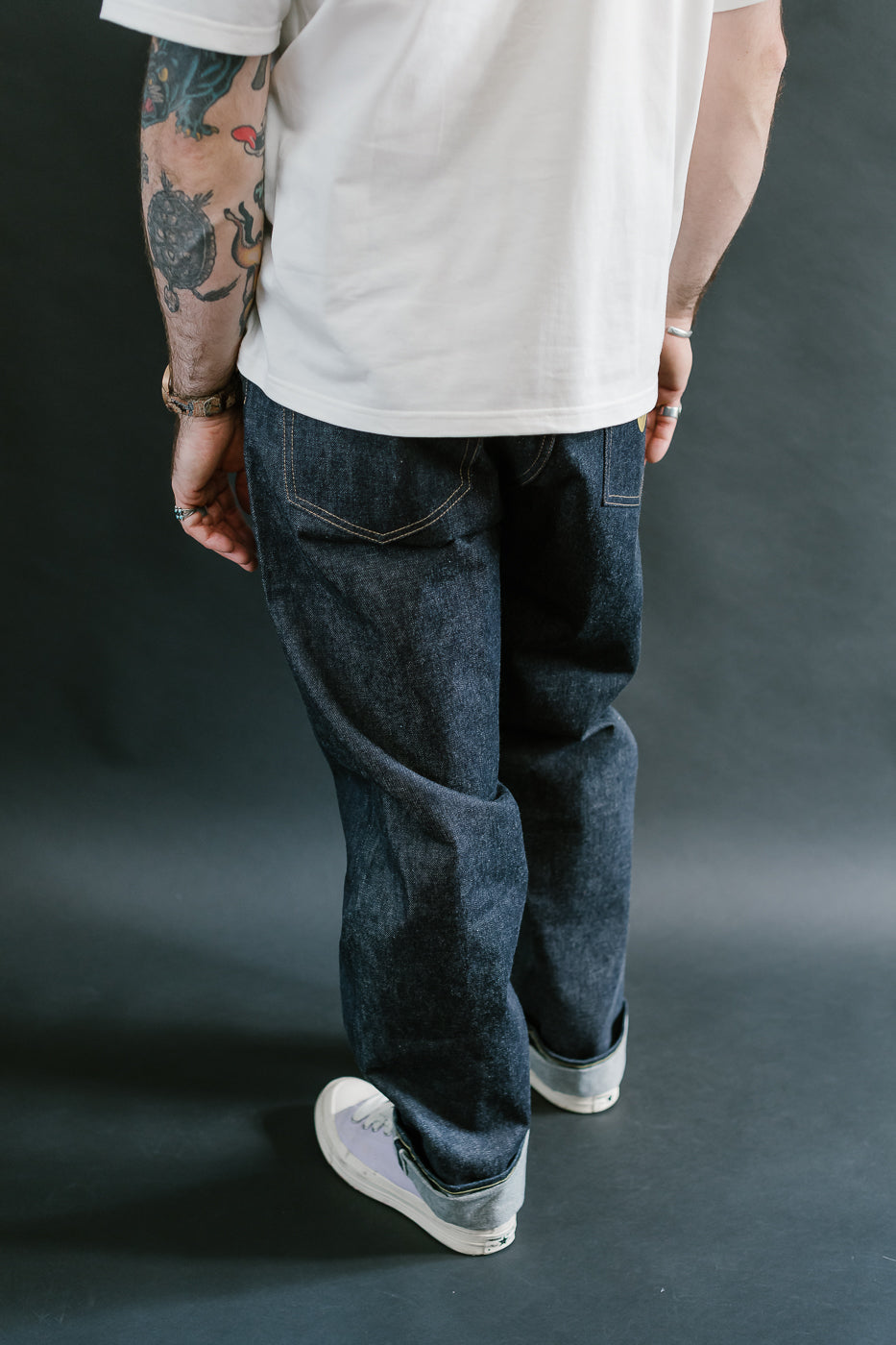 Person wearing a white t-shirt and dark blue jeans on a dark background