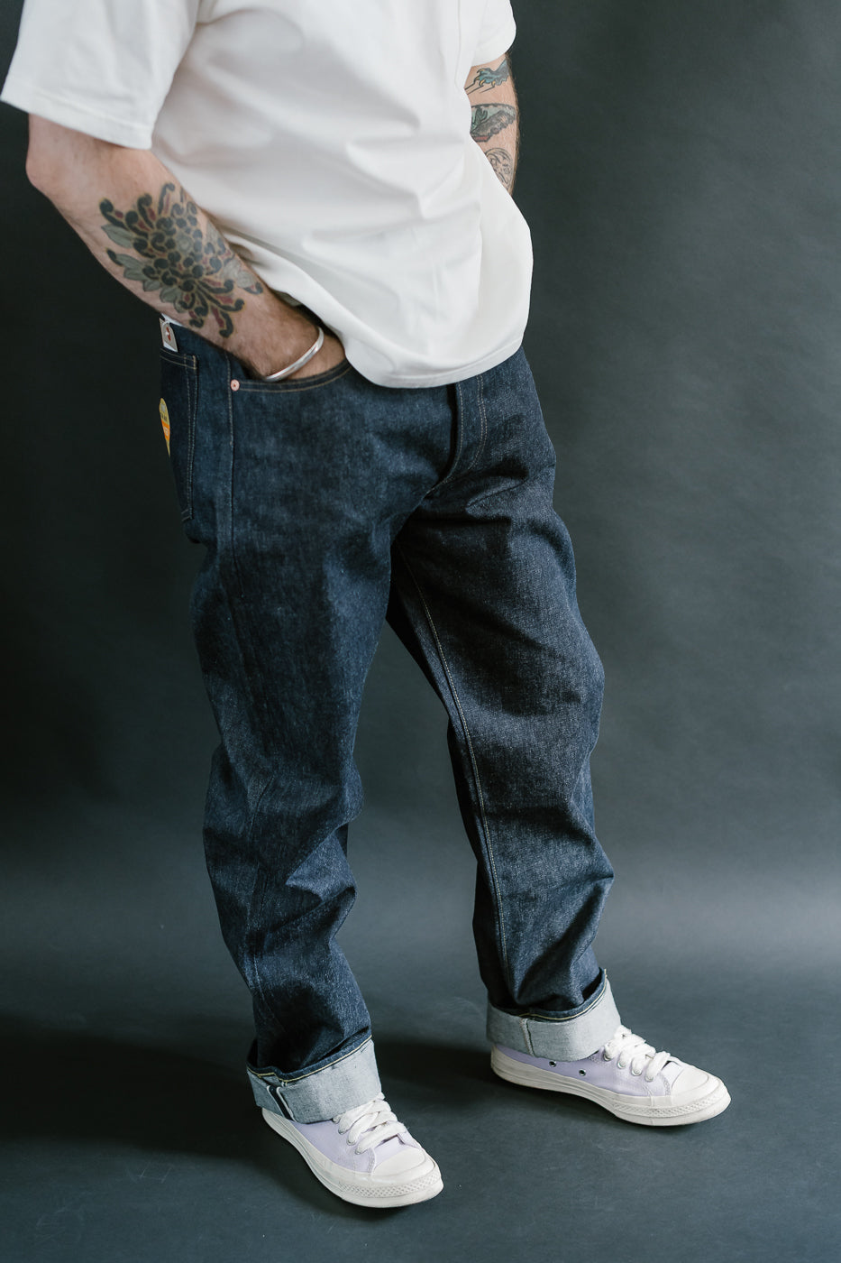 Person wearing dark blue jeans and white sneakers on a dark background