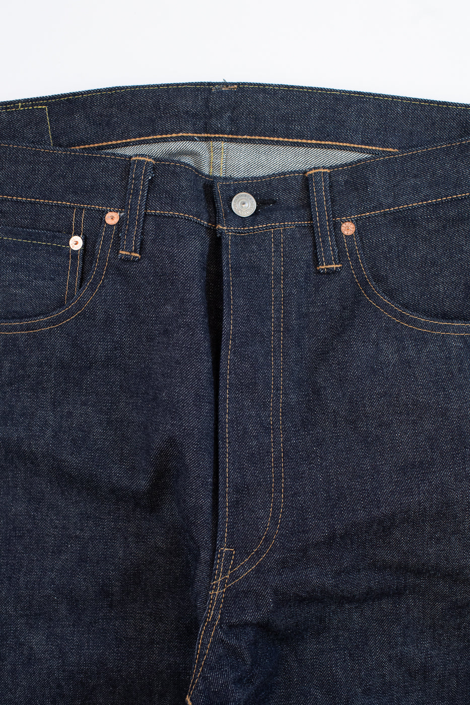 Close-up of dark blue denim jeans with stitching details on a white background