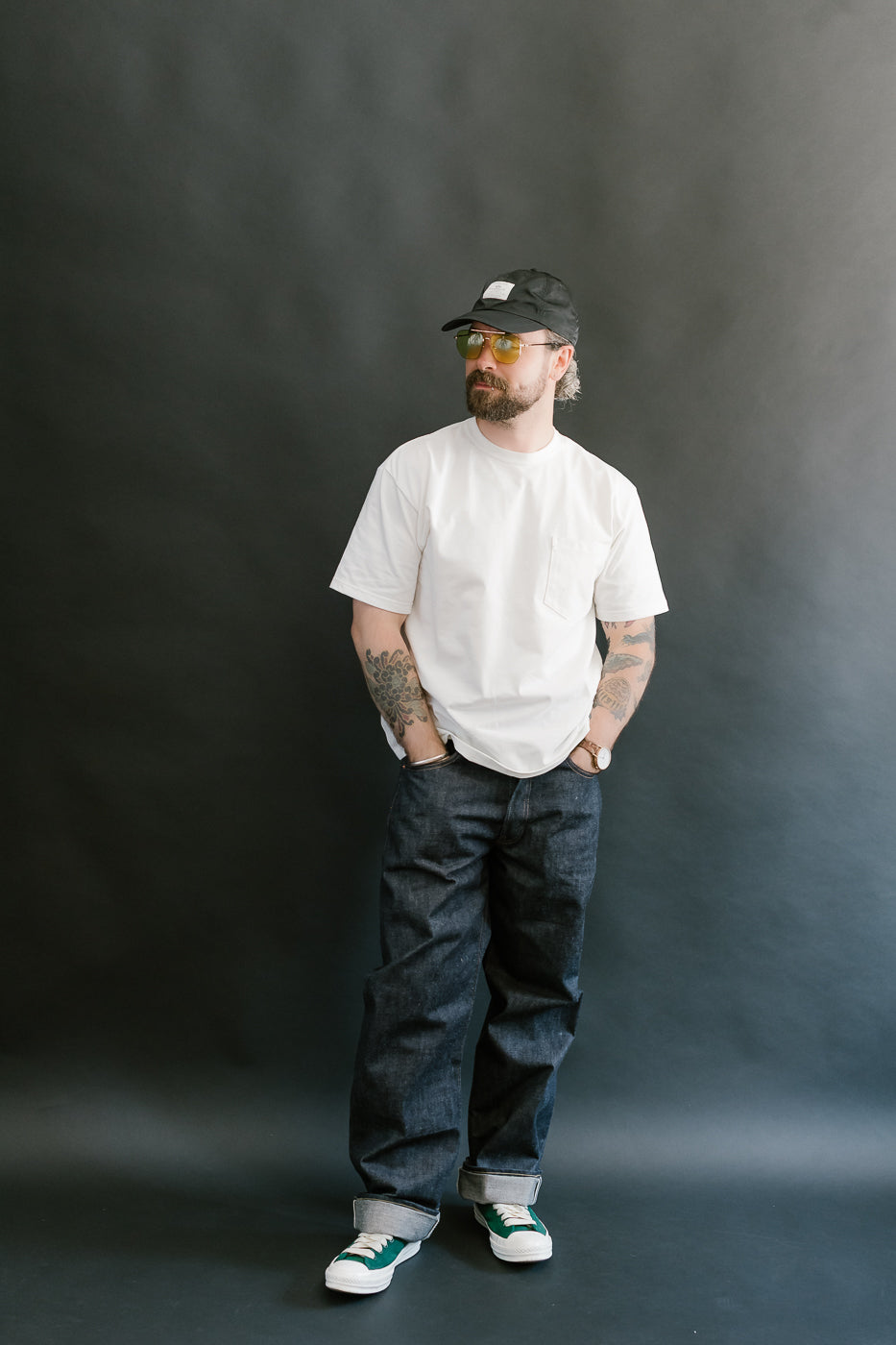 Man wearing a white t-shirt, dark jeans, and a cap against a black background