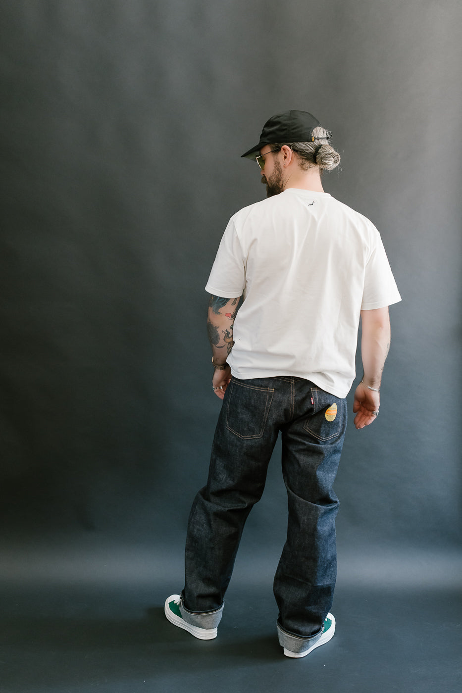 Man wearing a white t-shirt and dark jeans standing against a gray background