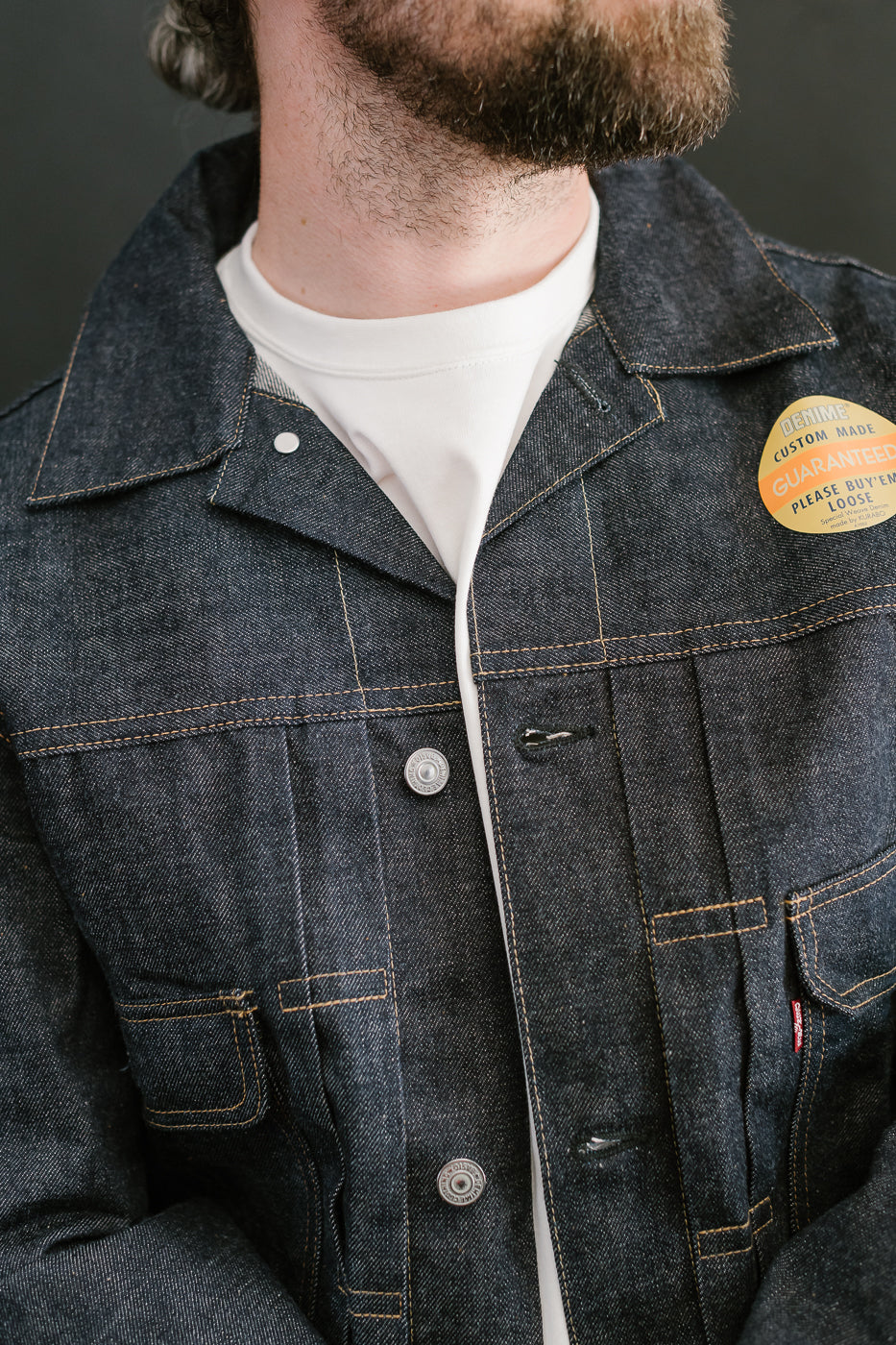Person wearing a denim jacket with a visible button and patch on a dark background