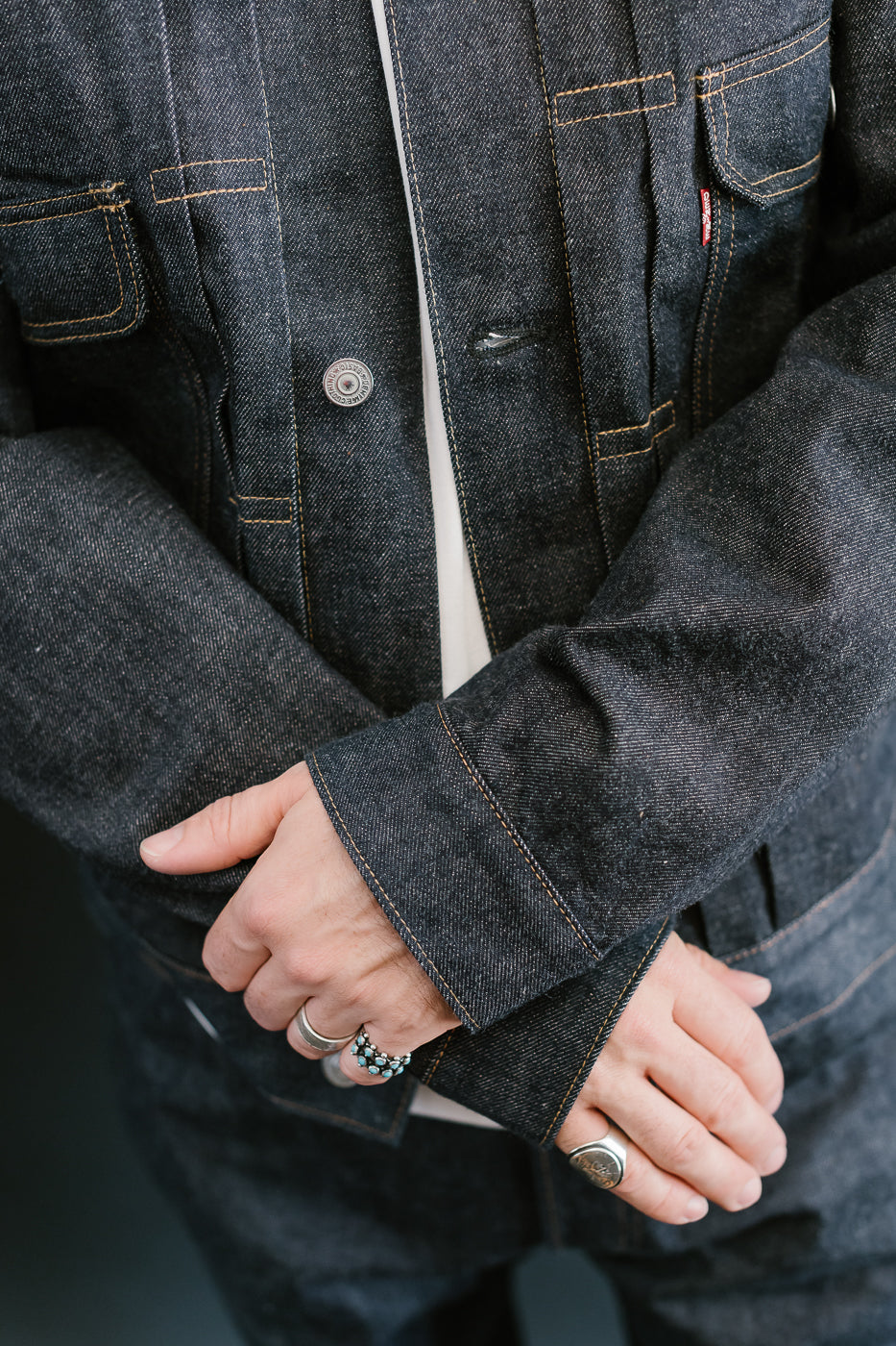 Close-up of a person wearing a dark denim jacket with visible buttons and a ring.