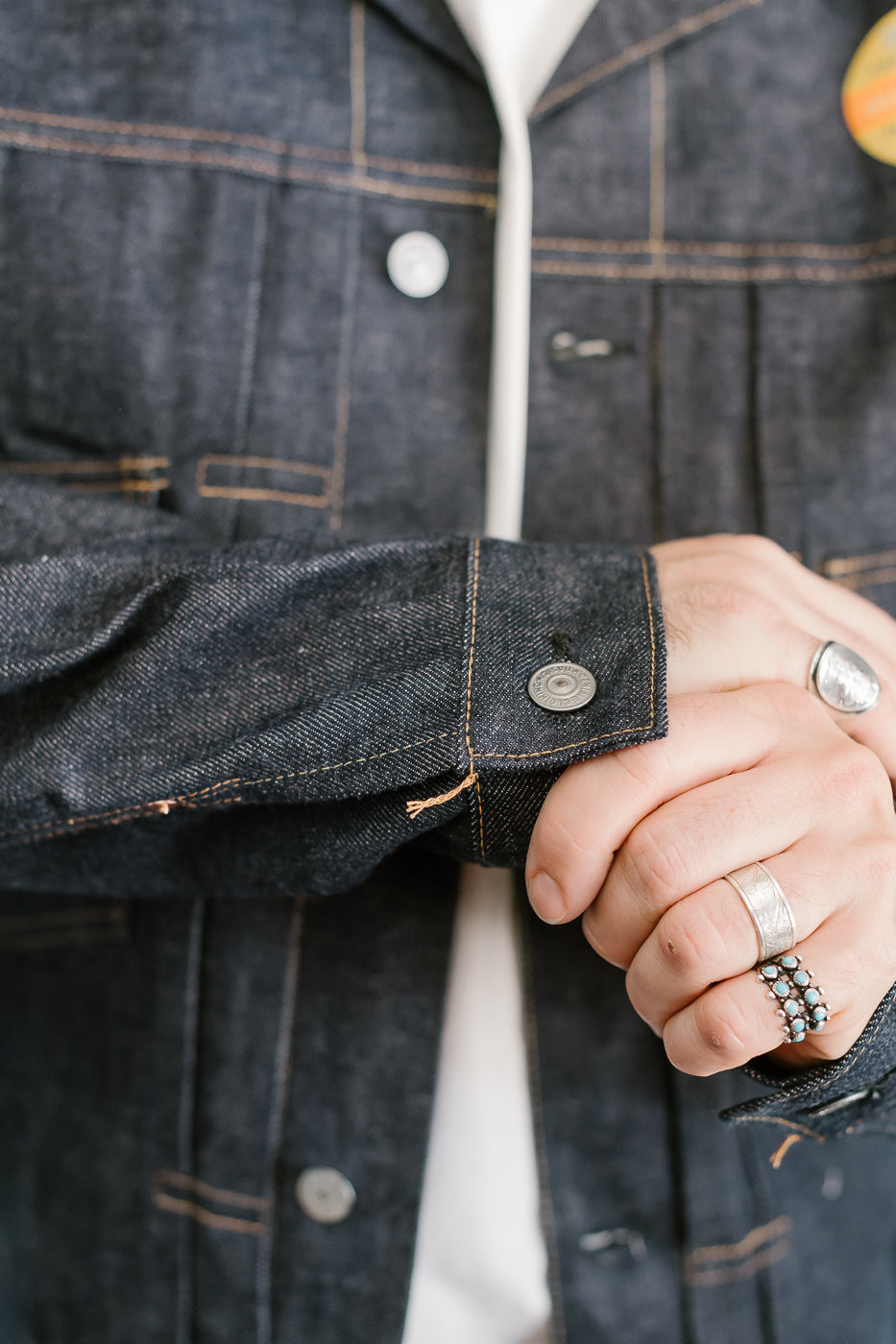 Person wearing a dark denim jacket with visible buttons and a white shirt underneath.