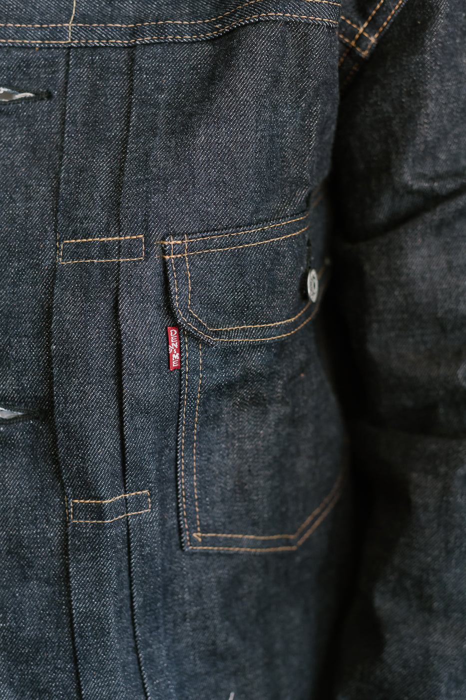 Close-up of a dark blue denim jacket with a brand logo on the pocket.