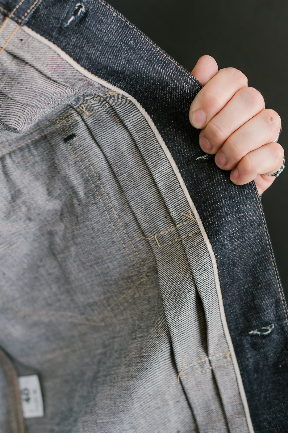 Close-up of a hand holding a gray denim jacket with a brand label.