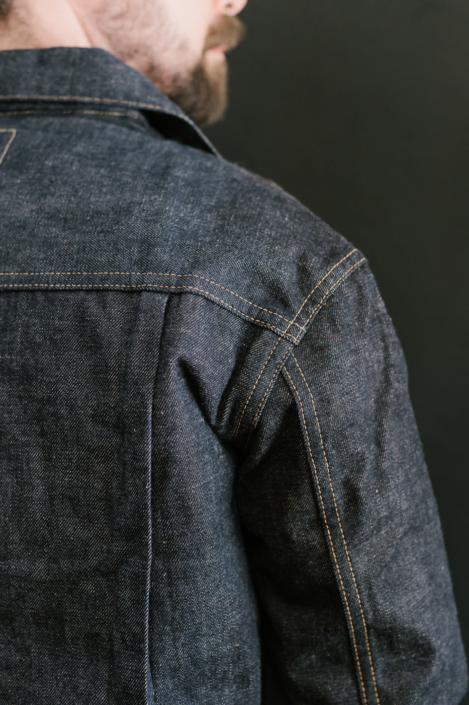Close-up of a person wearing a dark denim jacket against a black background