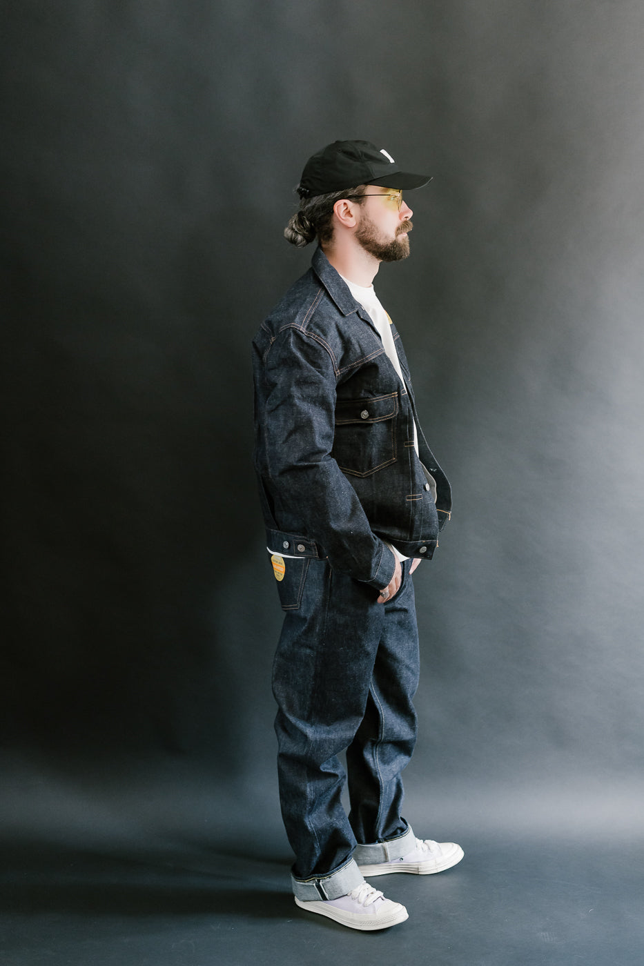 Man wearing a dark denim outfit with a cap against a gray background