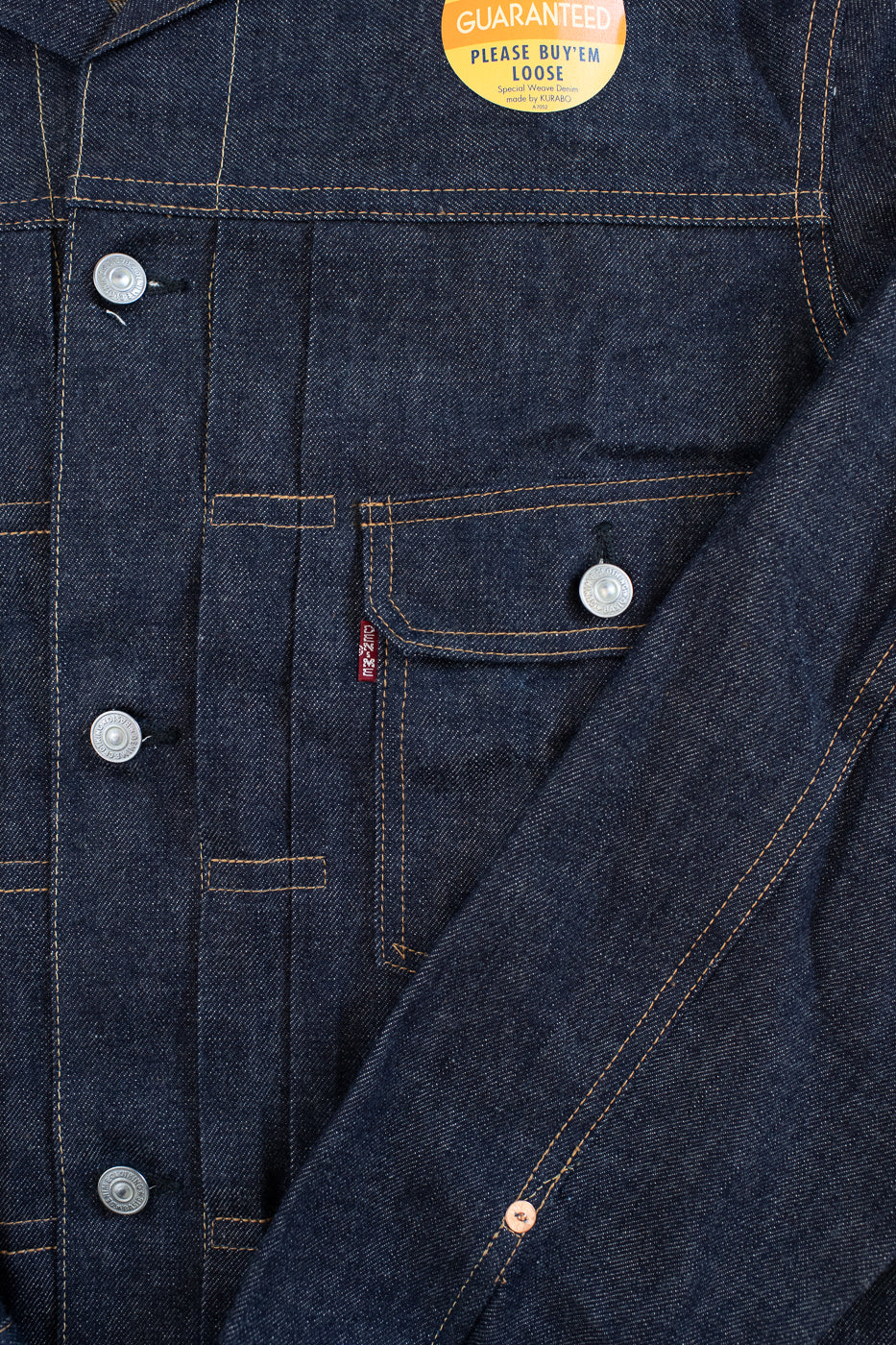 Close-up of a blue denim jacket with a button and a visible brand tag.