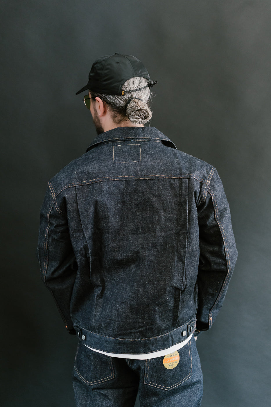Person wearing a dark denim jacket and cap against a gray background