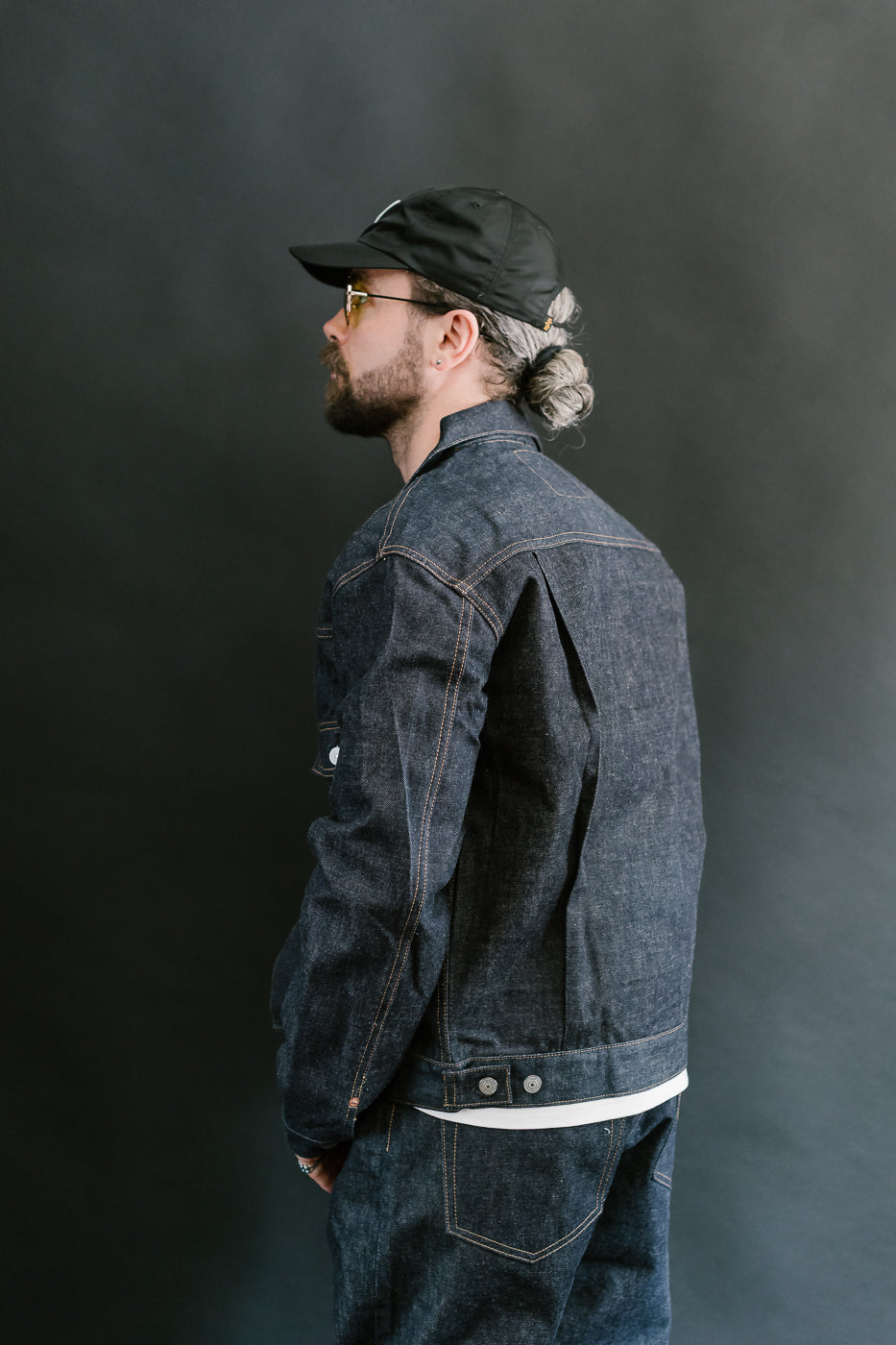 Man wearing a dark denim jacket and cap against a gray background