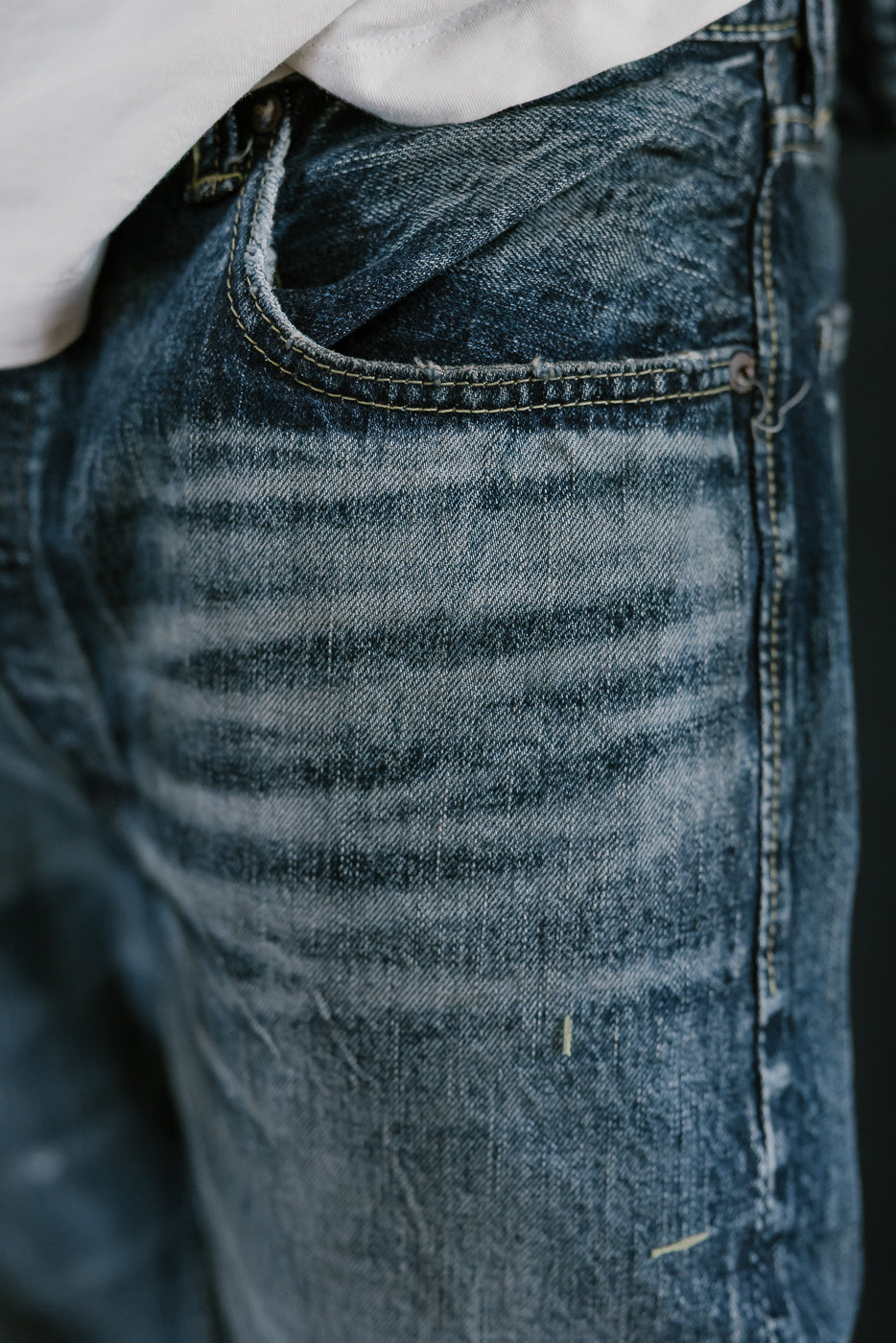 Close up of heavily washed denim jeans left pocket and whiskers.