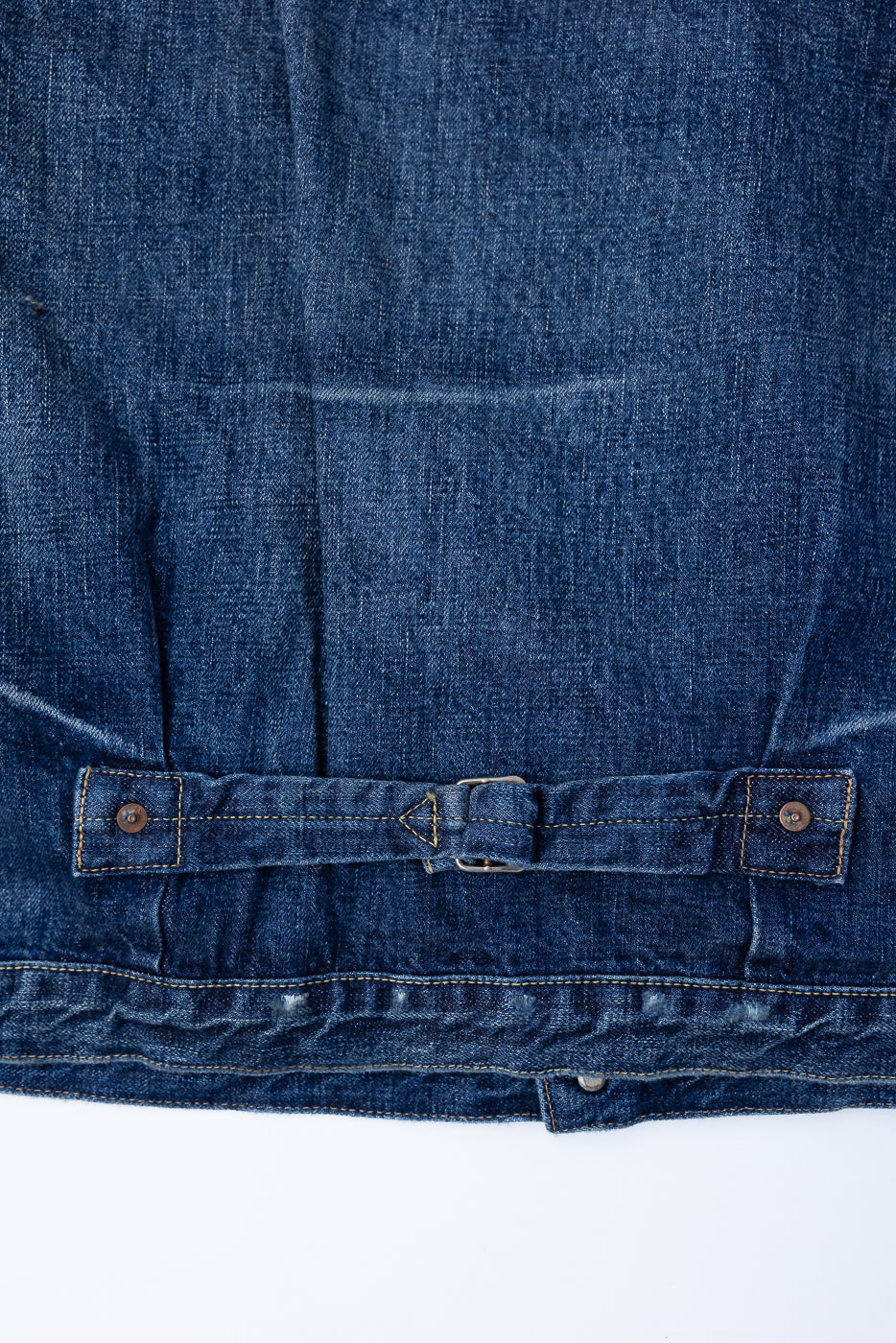 Heavily washed indigo denim jacket with a visible full count label on the left chest pocket on a white background, close up of cinch back.