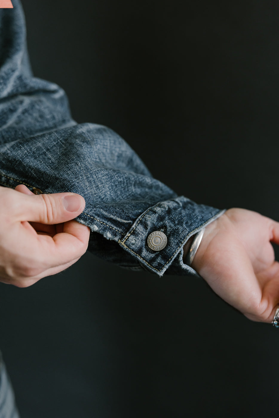 Bearded man wearing Heavily washed indigo denim jacket. Shot of donut button on interior side of cuff.