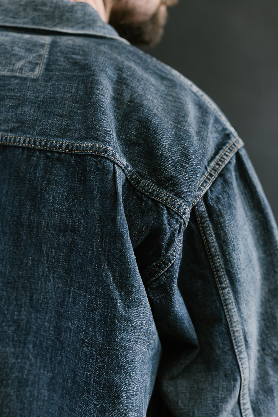 Bearded man wearing Heavily washed indigo denim jacket. Close up of shoulder seam.