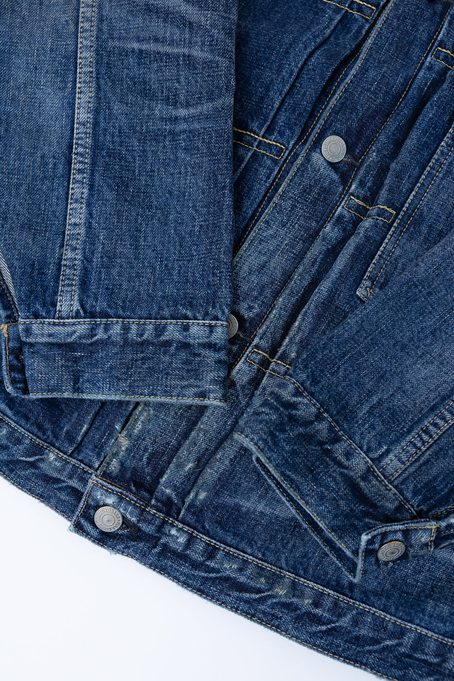 Heavily washed indigo denim jacket with a visible full count label on the left chest pocket on a white background, close up of denim fading, aging and cuffs.