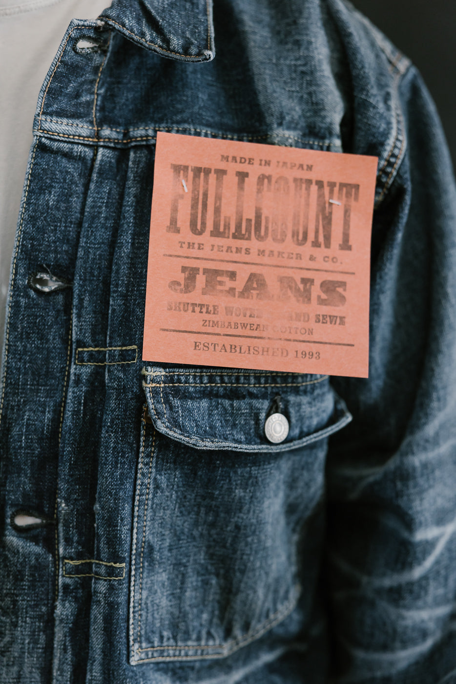 Bearded man wearing Heavily washed indigo denim jacket with a visible full count label on the left chest pocket. Close up of Fullcount branded tag, large red attached above the pocket.