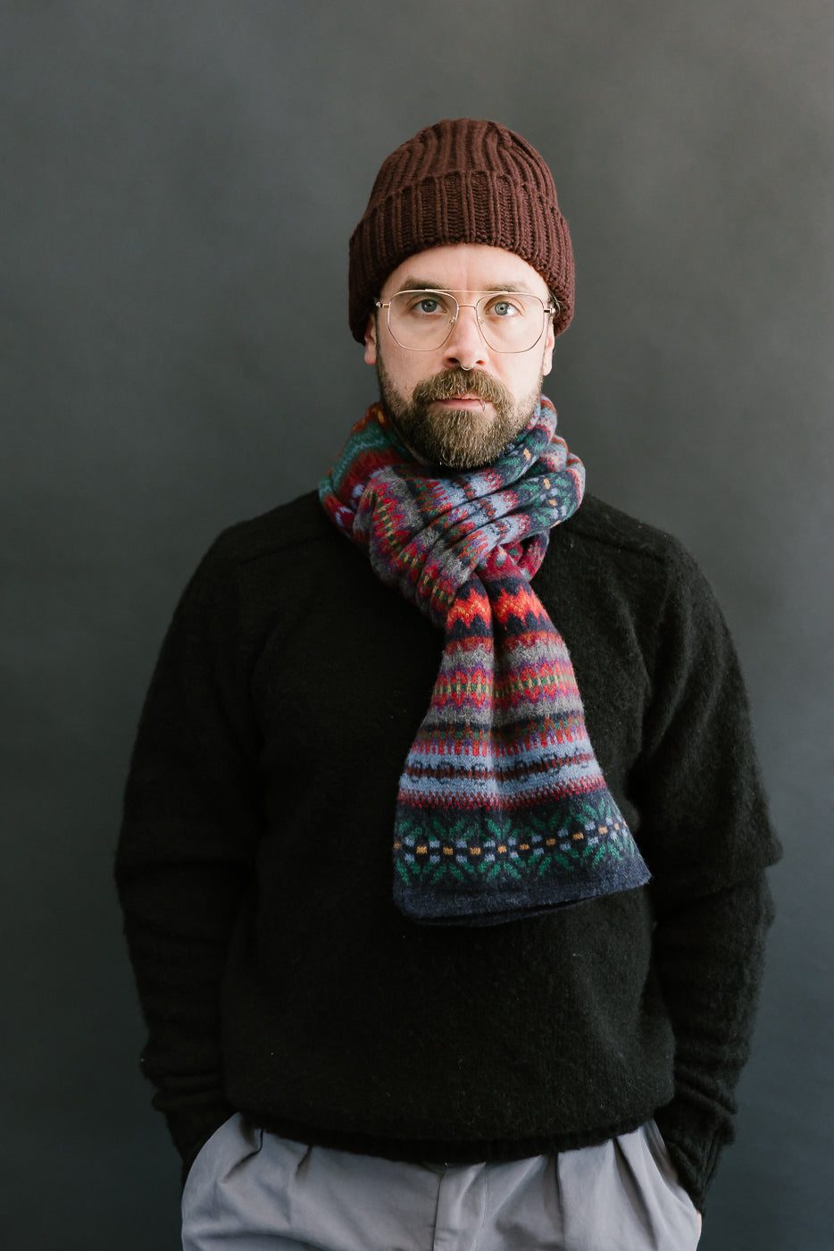 multicolored, patterned wool scarf with a navy base on a bearded man with a chocolate beanie, front view