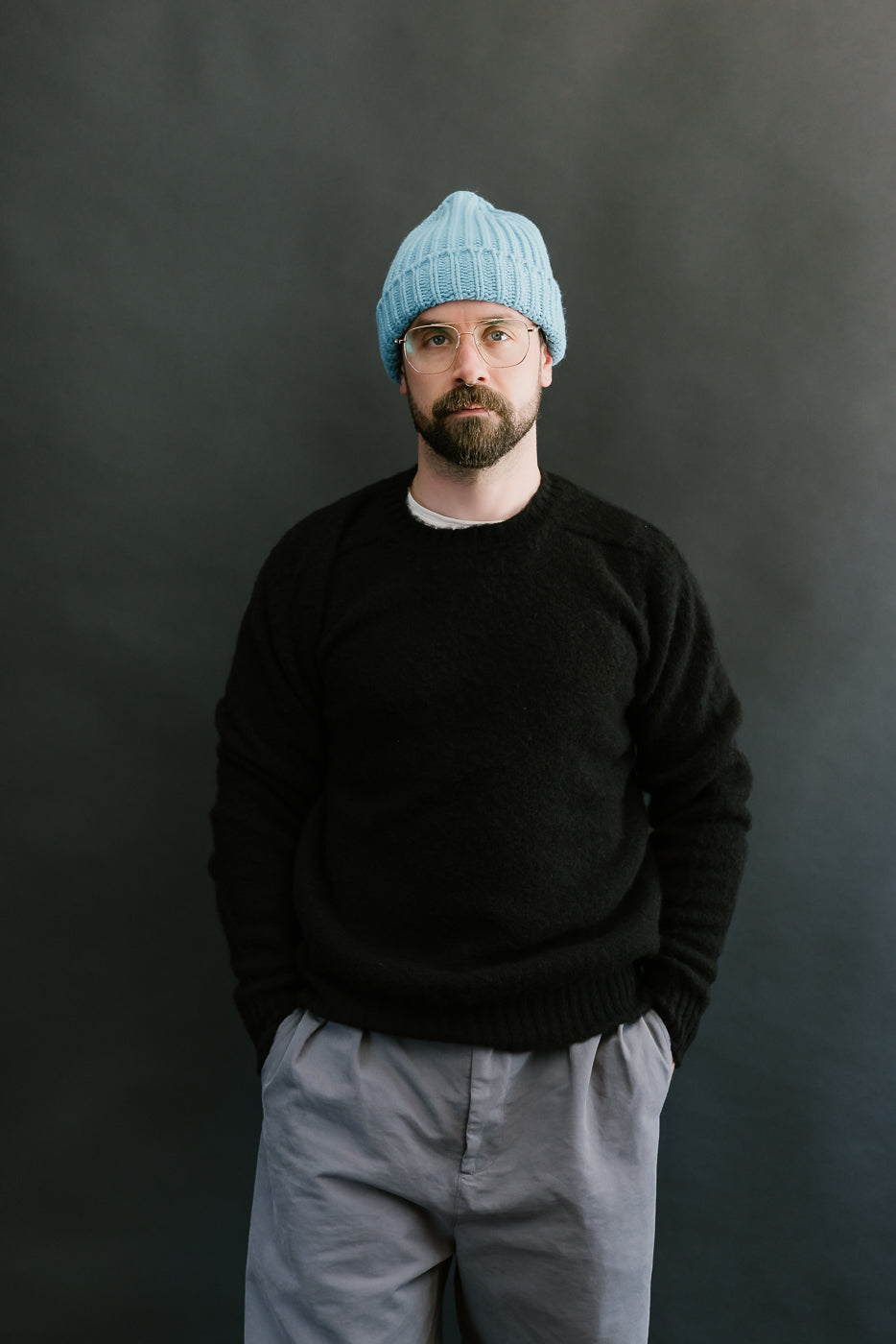 Man wearing a black sweater and light blue beanie against a dark background
