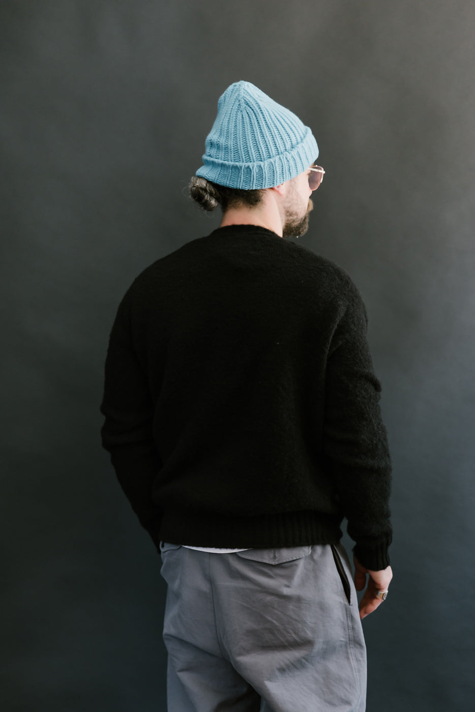 Person wearing a black sweater and light blue beanie against a dark background
