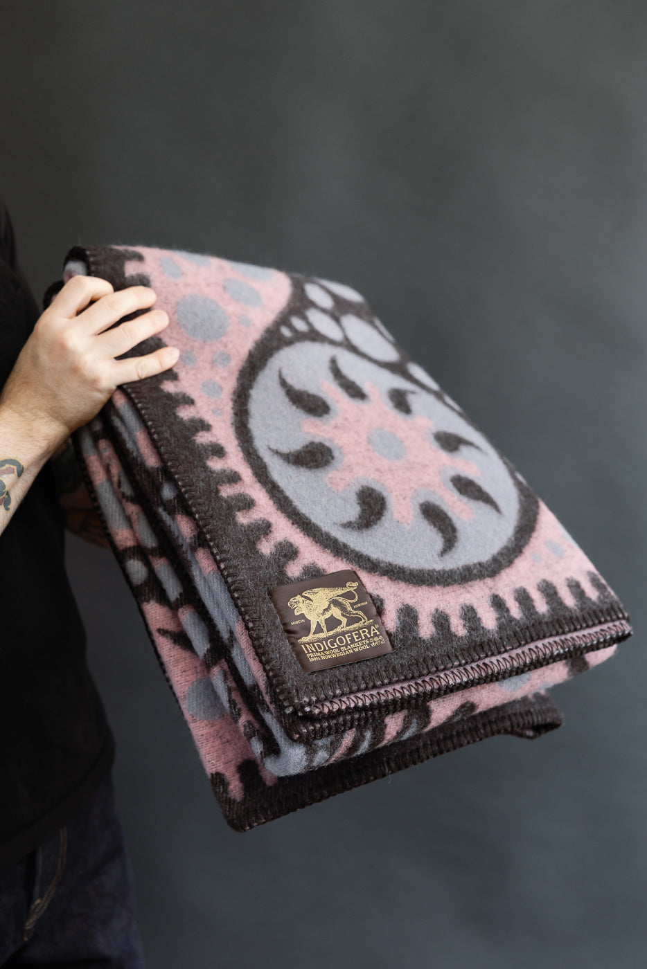 Person holding a patterned pink and black blanket with a logo on a dark background