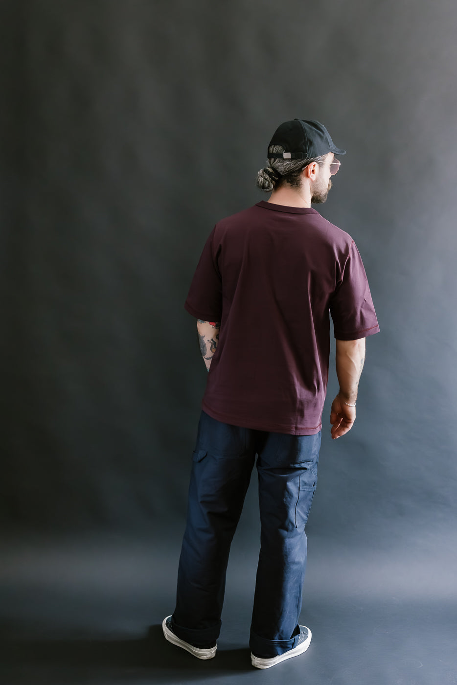 Person wearing a maroon t-shirt and blue jeans against a dark gray background