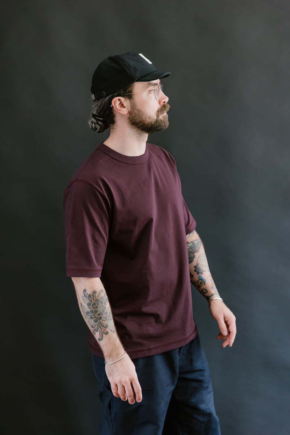 Man wearing a maroon t-shirt and black cap against a dark background
