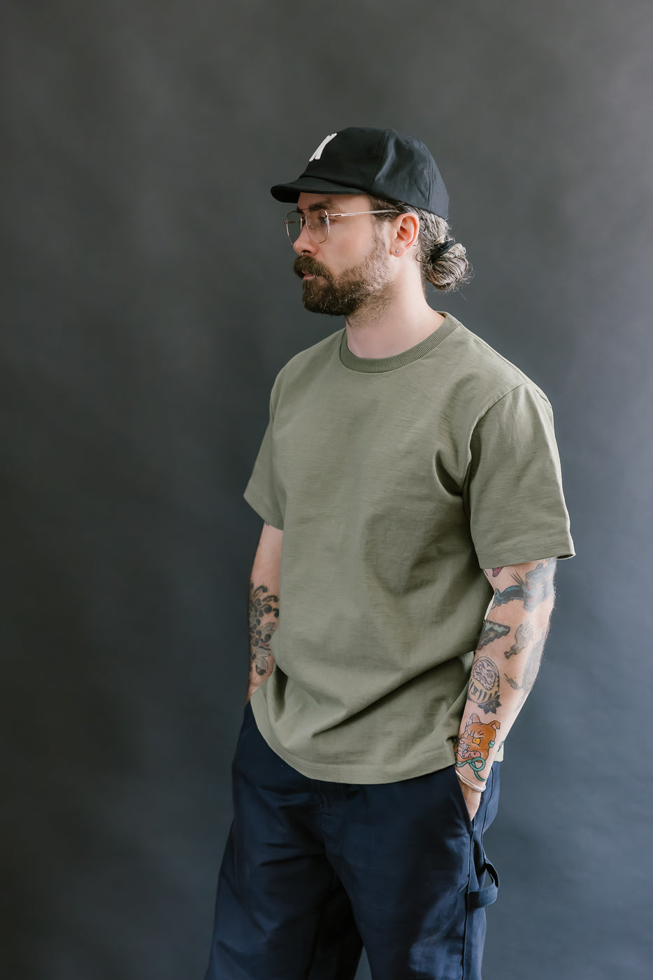 Man wearing a green t-shirt and black cap against a gray background