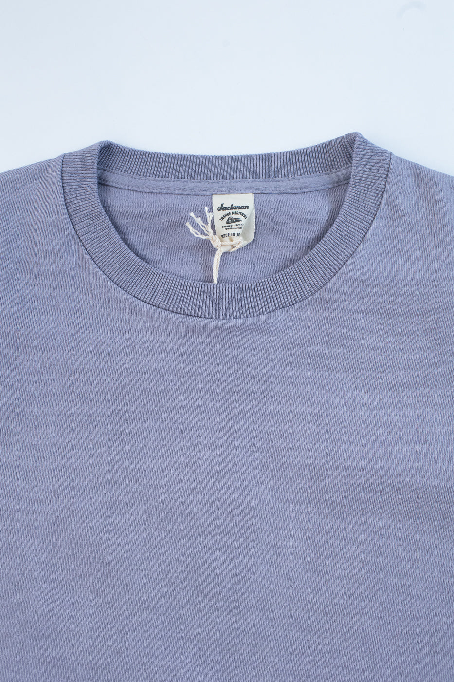 Close-up of a light purple t-shirt with a brand tag on a light blue background