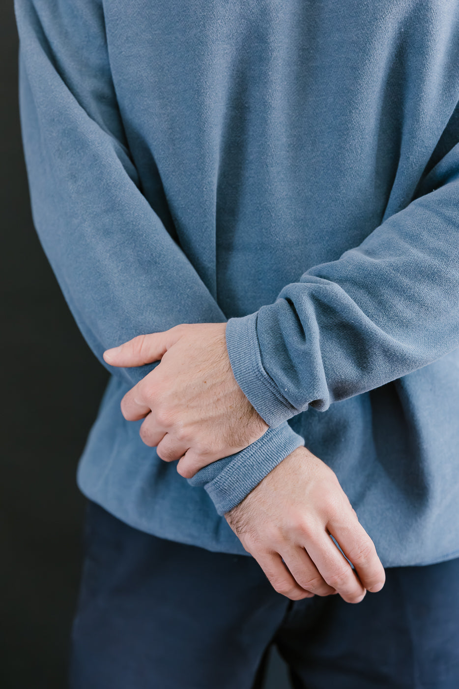 Person wearing a blue sweater with a close-up of their hands.