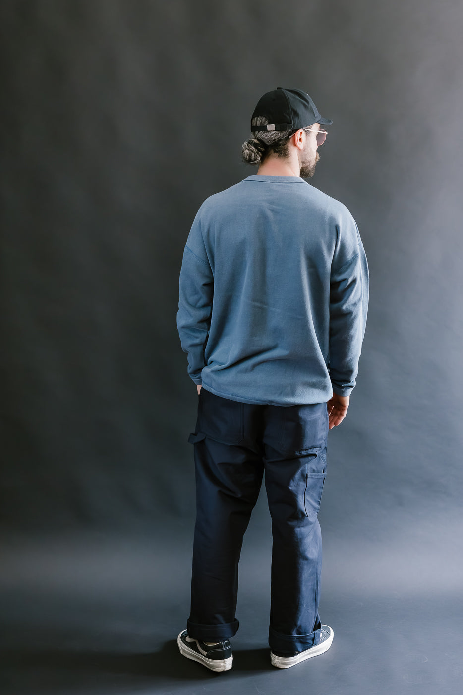 Person wearing a blue sweatshirt and dark pants standing against a gray background