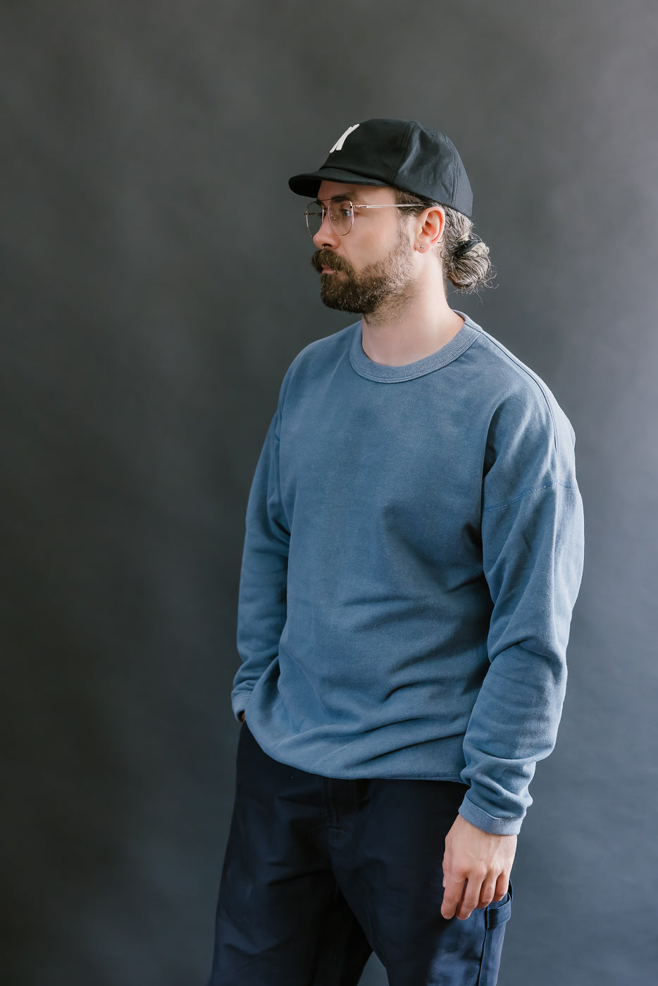 Man wearing a blue sweatshirt and black cap against a gray background